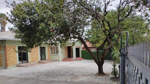 Un patio empedrado con un árbol, un edificio con puerta verde y una valla.