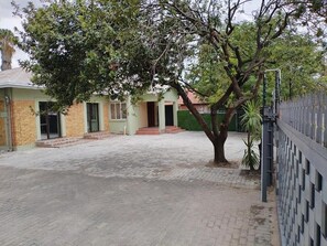 A paved courtyard with a tree, a building with a green door, and a fence. - Laroza Guest House (Rustenburg)