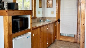 Eine kleine Küche mit Holzausstattung, einer Mikrowelle, einem Kühlschrank, einem Spülbecken und einem Fenster mit Jalousien.