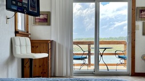 Ein Schlafzimmer mit einem großen Bett, einem an der Wand befestigten Fernseher, einer Glastür zum Außenbereich und Blick zum Himmel.