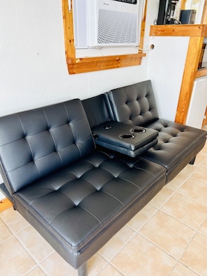 Un canapé en cuir noir avec une structure en bois, une petite table et un appareil de climatisation blanc fixé au mur.