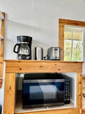 Cuina amb cafetera, torradora i microones sobre una estant de fusta.