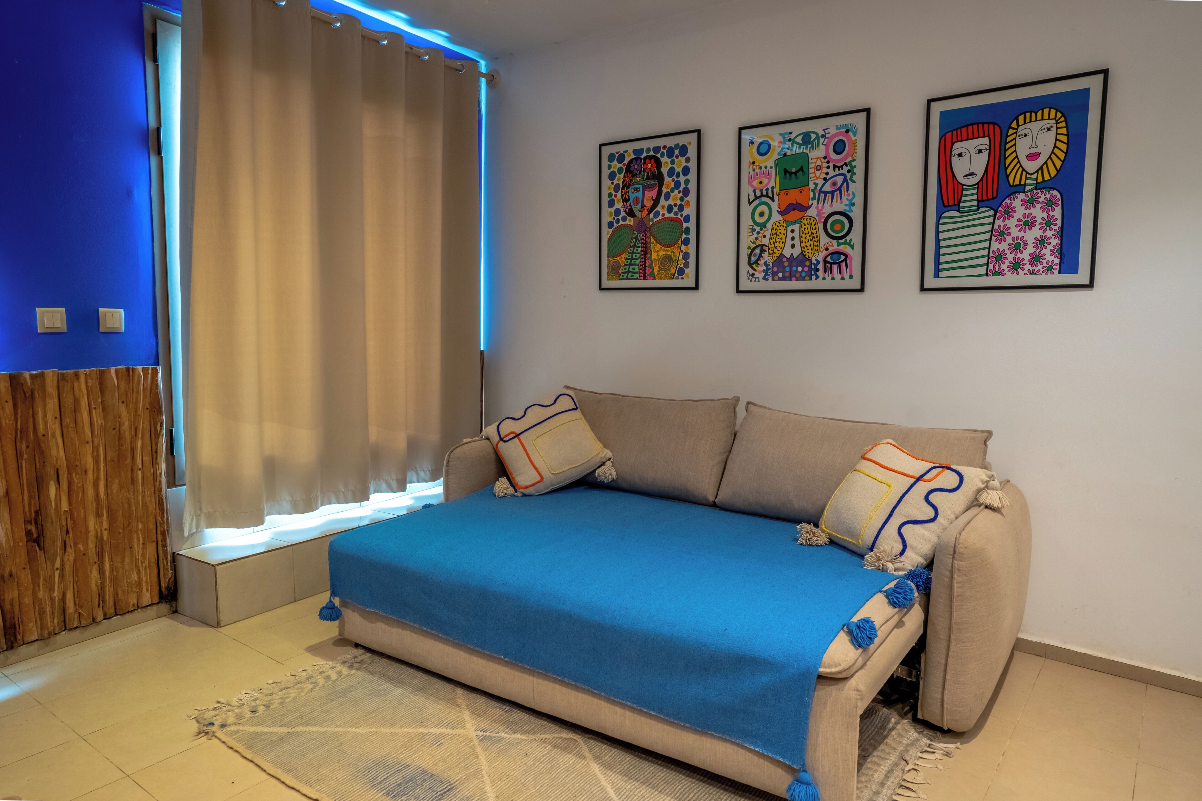 Een kamer met een bank, een raam met gordijnen en drie ingelijste kunstwerken aan de muur.