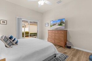Ein Schlafzimmer mit einem Bett, einem Schminktisch, einem Fernseher und einer Schiebetür, die auf eine Terrasse führt.