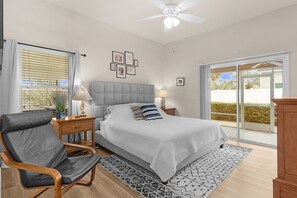 Ein Schlafzimmer mit Bett, Stuhl, Schreibtisch, Lampe und Deckenventilator.