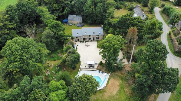 Vue aérienne d’une propriété comprenant une grande maison, une piscine et un jardin luxuriant.