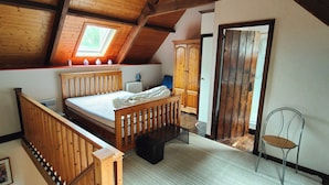 Ein Schlafzimmer mit schrägen Wänden, einem Bett, einem Holzschrank, einem Stuhl und einer Heizung.