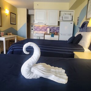 Ein Hotelzimmer mit zwei Betten, einer Küchenzeile, einem Esstisch und einer Wandleuchte.