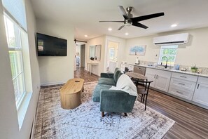 A modern living room with a sofa, coffee table, and a TV. There is a kitchen area with cabinets and a dining table. - Modern,Cozy Farm Cabin with Lake/Beach/dock access (Eustis)