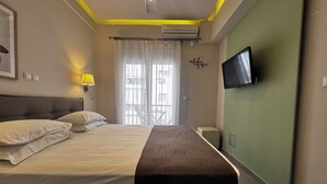 A hotel room with a bed, a TV mounted on the wall, a window with curtains, and an air conditioning unit. - Athens Stay 15 Hotel-Style Room & King Bed (Athina)