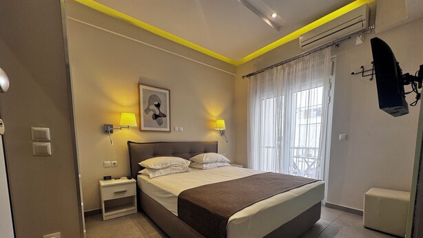 A modern hotel room with a large bed, bedside lamps, a small table, and a view of the outdoors. - Athens Stay 15 Hotel-Style Room & King Bed (Athina)