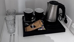 A coffee station with a coffee maker, two cups, a glass, and a packet of coffee. - Athens Stay 15 Hotel-Style Room & King Bed (Athina)