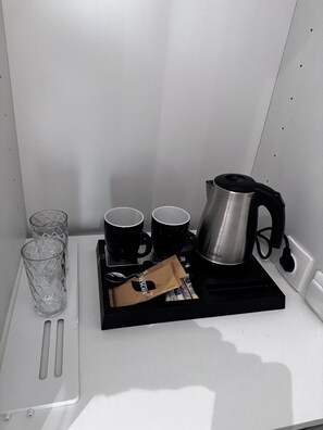 Eine Kaffeestation mit Kaffeemaschine, zwei Tassen, einem Glas und einer Kaffeepackung.