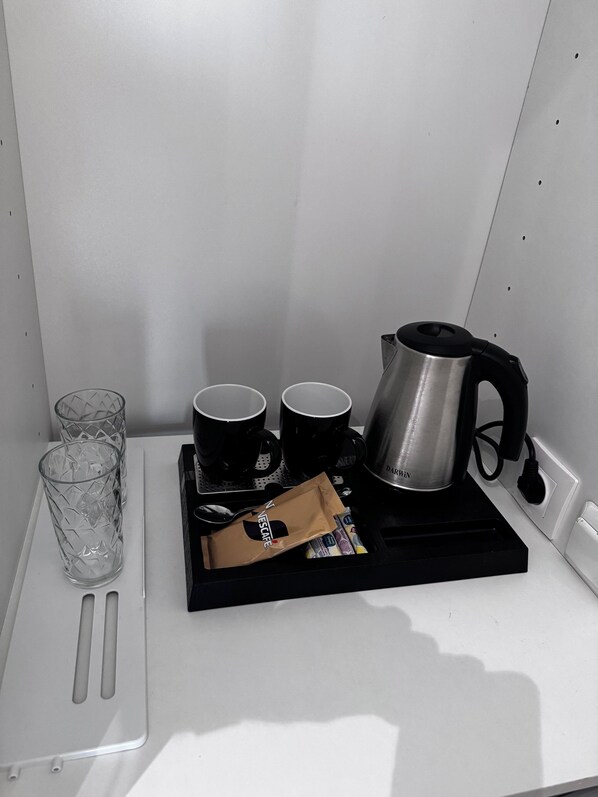 A coffee station with a coffee maker, two cups, a glass, and a packet of coffee.