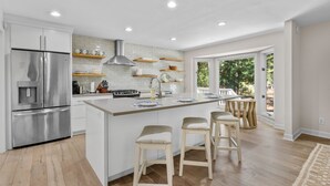 Une cuisine moderne dotée d’un îlot central, d’appareils électroménagers en acier inoxydable et offrant une vue sur l’extérieur.