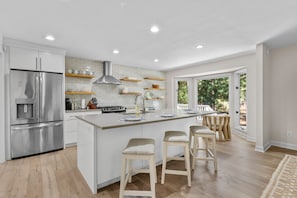 A modern kitchen with a central island, stainless steel appliances, and a view to the outdoors. - Seabrook Exclusives | 2963 Seabrook Island Rd (Seabrook Island)