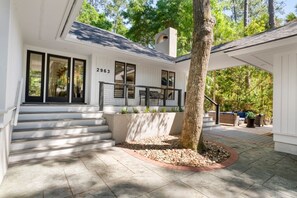 A modern house with a number '2963' on the wall, a staircase leading to a porch, and a tree in the center. - Seabrook Exclusives | 2963 Seabrook Island Rd (Seabrook Island)