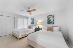 A bedroom with two beds, a ceiling fan, a nightstand with a lamp, and a closet. - Seabrook Exclusives | 2963 Seabrook Island Rd (Seabrook Island)