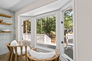 A room with wicker chairs, a white brick wall, and large windows overlooking a deck and trees. - Seabrook Exclusives | 2963 Seabrook Island Rd (Seabrook Island)