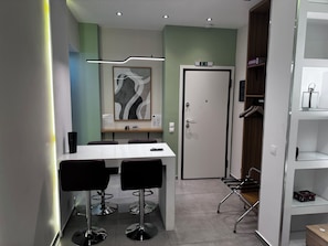 A modern dining area with a white table, black chairs, a framed abstract artwork, and a door with a sign above it. - Athens Stay 35 (Athina)