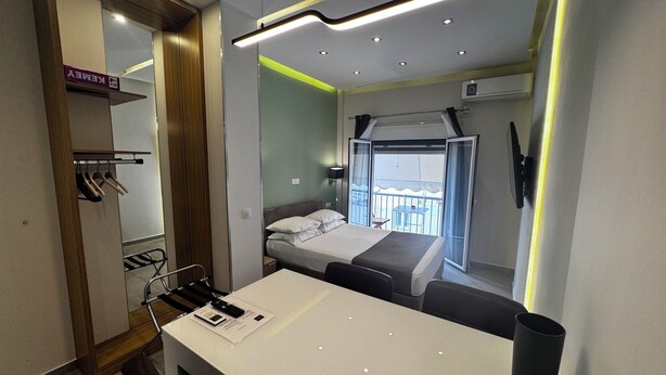 Ein modernes Hotelzimmer mit Bett, Schreibtisch, Stuhl, Kleiderschrank und einem Balkon mit Tisch und Stühlen.