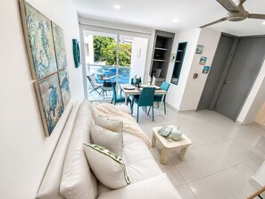 Ein modernes Wohnzimmer mit einer Couch, einem Essbereich mit Stühlen, einem Deckenventilator und Blick durch eine Glastür.