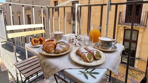 A balcony with a table set for breakfast, including pastries and coffee, overlooking a building with balconies. - Duomo 31 Loft · Catania Centre Balcony & Cathedral (Catania)