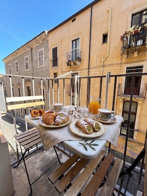 A balcony with a table set for breakfast, including pastries and coffee, overlooking a building with balconies. - Duomo 31 Loft · Catania Centre Balcony & Cathedral (Catania)