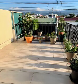 Tagterrasse med krukker med planter, gelænder og udsigt til bygninger og fjerne bjerge.
