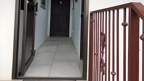 Um corredor com uma porta que dá para um quarto, um corrimão vermelho e uma luminária no teto.