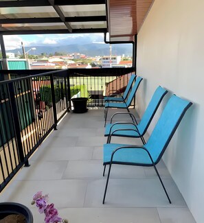 En balkon med blå stole, en potteplante og udsigt til bygninger og bjerge.