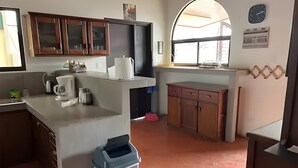 Uma cozinha com cafeteira, lixeira, armários de madeira e um relógio na parede.