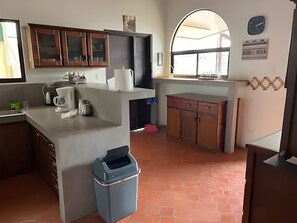 Eine Küche mit Kaffeemaschine, Mülleimer, Holzschränken und einer Uhr an der Wand.