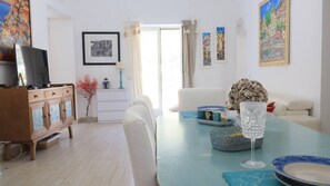 Een eethoek met een tafel gedekt voor twee personen, een televisie op een houten kast, en kunstwerken aan de wanden.