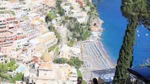 Un pueblo costero con playa, edificios y un árbol destacado.