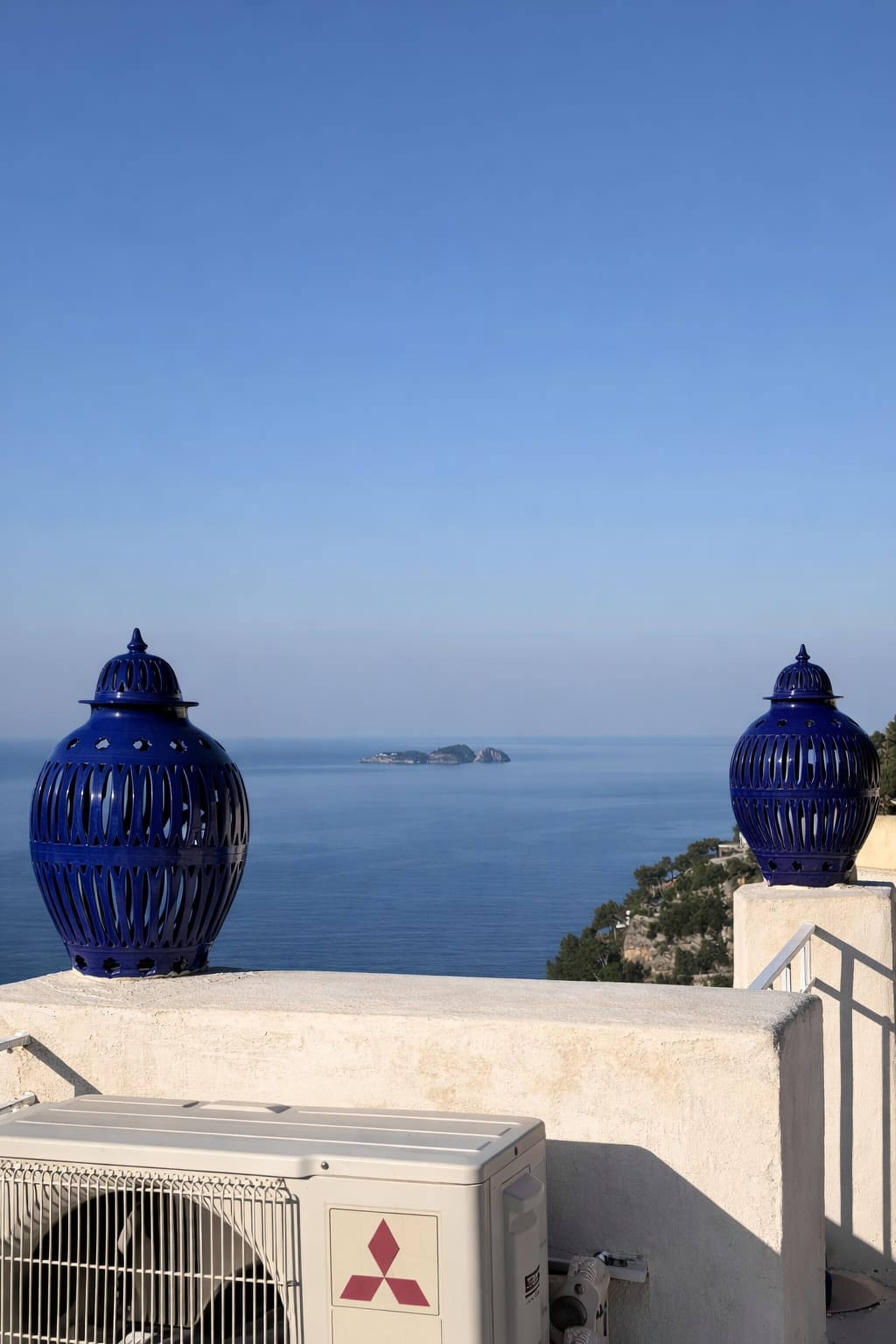 Vista mare con due grandi lanterne blu su un balcone, un condizionatore Mitsubishi e un'isola in lontananza.