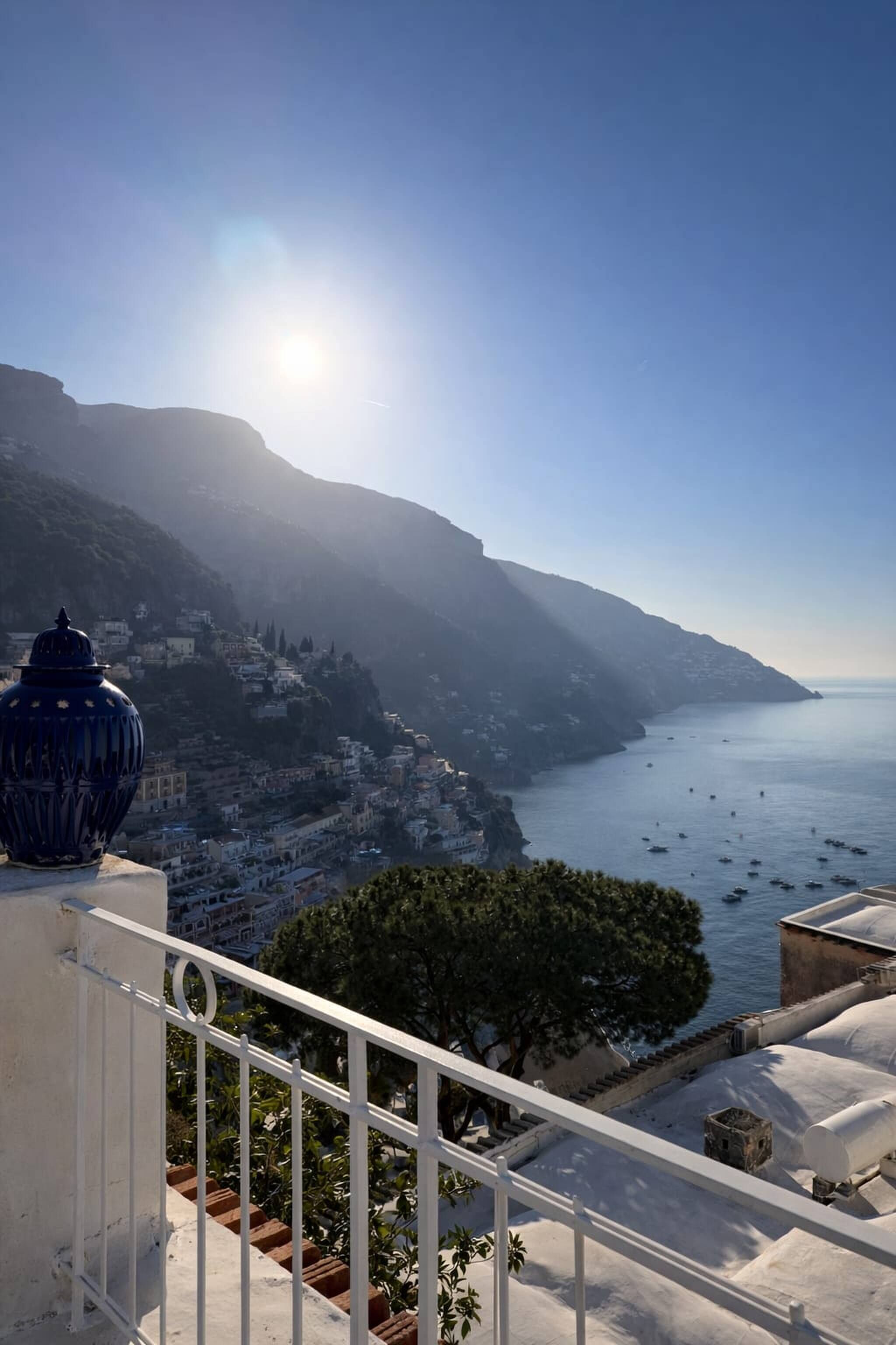 Une vue sur la côte, avec un ciel dégagé, un balcon doté d’une balustrade blanche et un pot en céramique bleue.