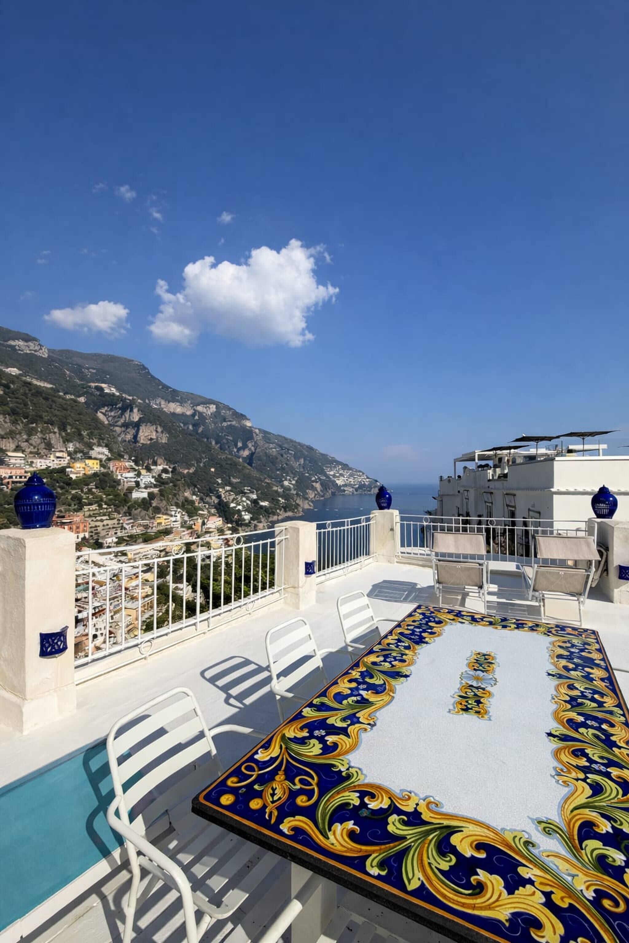 Um terraço no telhado com piscina, cadeiras brancas e uma mesa decorativa.