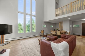 Ein geräumiges Wohnzimmer mit großem Fernseher, Ledersofa und einem Essbereich mit Holztischen und -stühlen.
