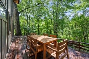 Eine Holzterrasse mit Tisch und Stühlen, umgeben von Bäumen.