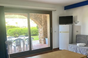 Ein Zimmer mit einer Schiebetür zu einer Terrasses, einem an der Wand befestigten Flachbildfernseher, einem Bett mit gestreifter Bettwäsche und einem kleinen Tisch.
