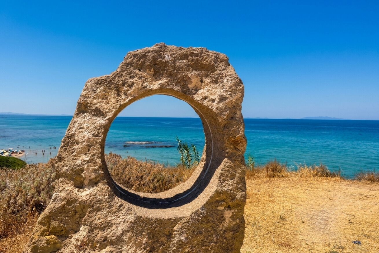 Une formation rocheuse naturelle présentant une ouverture circulaire, dominant une zone côtière aux eaux bleues et limpides et offrant une vue sur la terre ferme au loin.