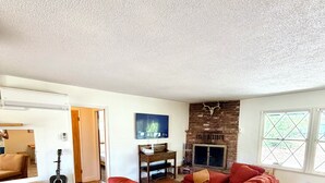 A living room with a red sofa, wooden flooring, a fireplace, and a TV. - 3-bedroom house in peaceful Sierras on 4.5 acres along road to Bass Lake (Wishon)