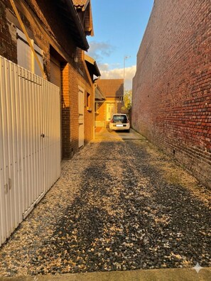 Une ruelle étroite avec un chemin de gravier, une voiture garée et une porte de garage blanche.