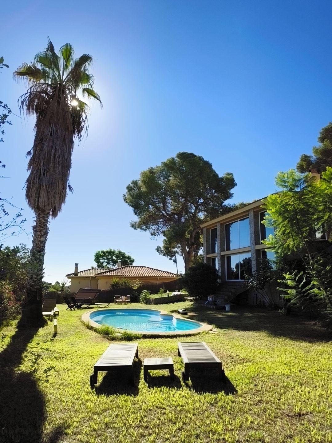 Um quintal com piscina, cadeiras de descanso e uma casa com telhado de cerâmica.