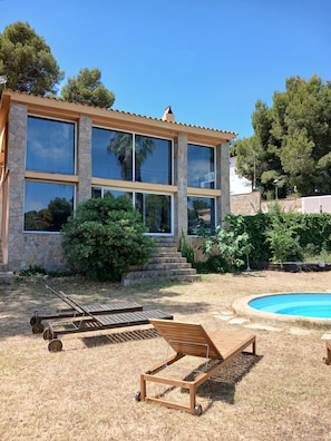Une maison moderne dotée de grandes fenêtres, d’une piscine et de mobilier d’extérieur.