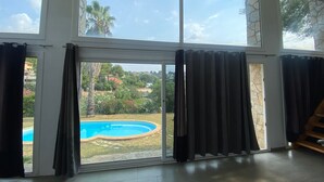 A room with large windows, a view of a swimming pool, and a stone wall. - Private pool and garden, near the beach, mountain hikes, Port Aventura. (Costa-Cunit)