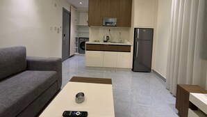 A modern living room with a sofa, a coffee table, a remote control, a kitchen area with appliances, and a dining table. - 105 JRE Apartment With Stunning Boulevar (Amman)
