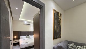 A modern hotel room with a bed, a sofa, a painting, and a door leading to another room. - 105 JRE Apartment With Stunning Boulevar (Amman)