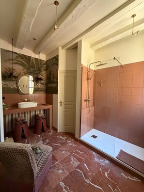 A bathroom with a marble floor, a sink, a mirror, a shower, and a door. - Vrbo Property (Chinon)